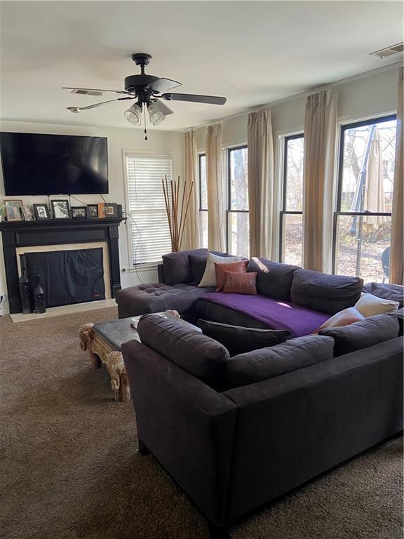 carpeted living area with ceiling fan, a glass covered fireplace, and visible vents