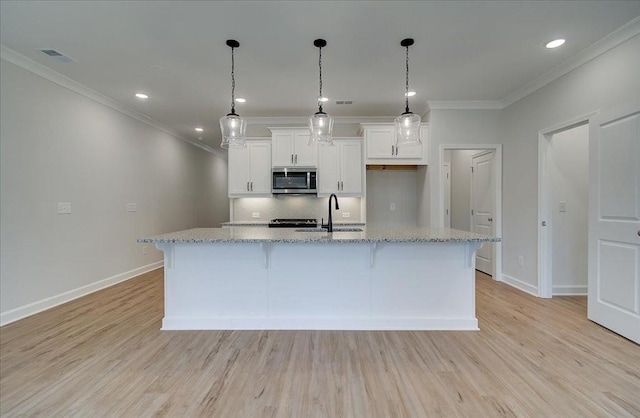 kitchen featuring light stone countertops, a large island with sink, and white cabinets