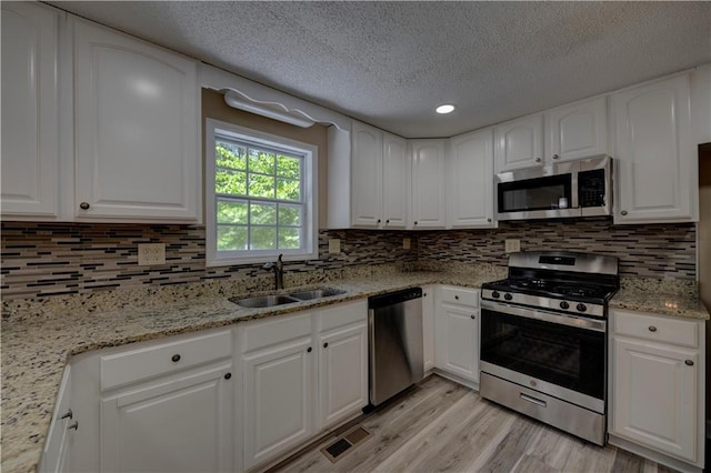 535 Toonigh Rd, Woodstock, GA 30188 - kitchen with appliances with stainless steel finishes, a sink, light wood finished floors, a textured ceiling, and decorative backsplash