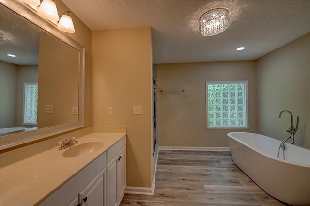 535 Toonigh Rd, Woodstock, GA 30188 - full bathroom with wood finished floors, vanity, a soaking tub, a textured ceiling, and baseboards