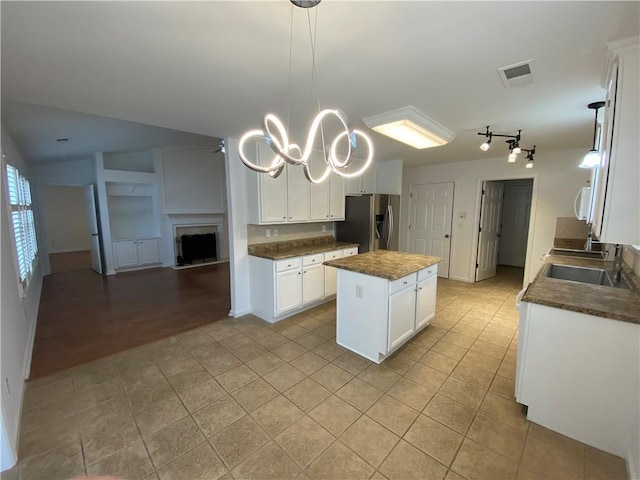 kitchen with a sink, stainless steel fridge, dark countertops, open floor plan, and a center island