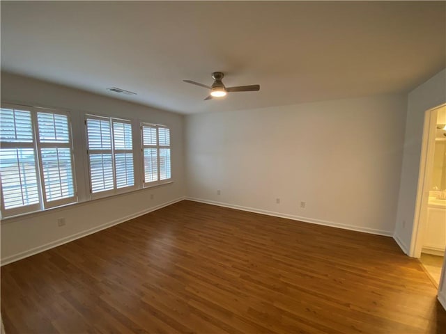 spare room featuring ceiling fan, visible vents, baseboards, and dark wood finished floors