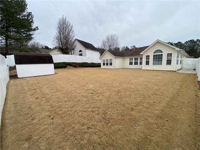 rear view of property featuring a gate, a yard, and a fenced backyard