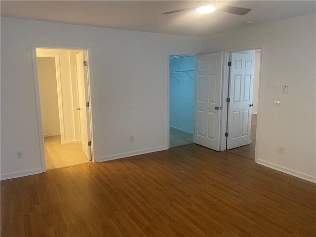 unfurnished bedroom featuring a spacious closet, wood finished floors, baseboards, and connected bathroom