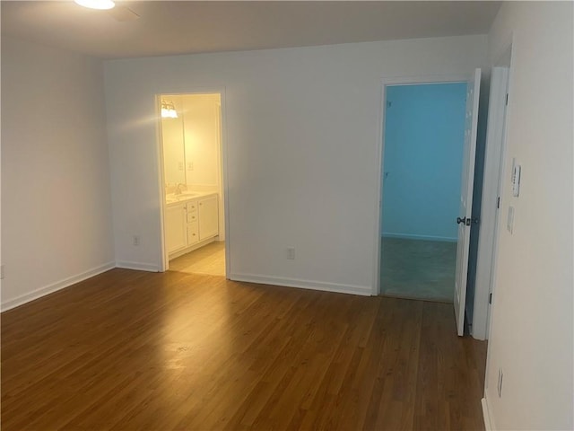 unfurnished bedroom featuring wood finished floors, baseboards, a sink, a spacious closet, and a closet