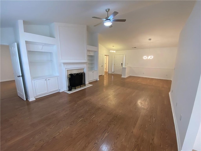 unfurnished living room featuring dark wood-type flooring, a fireplace with raised hearth, a ceiling fan, built in features, and vaulted ceiling