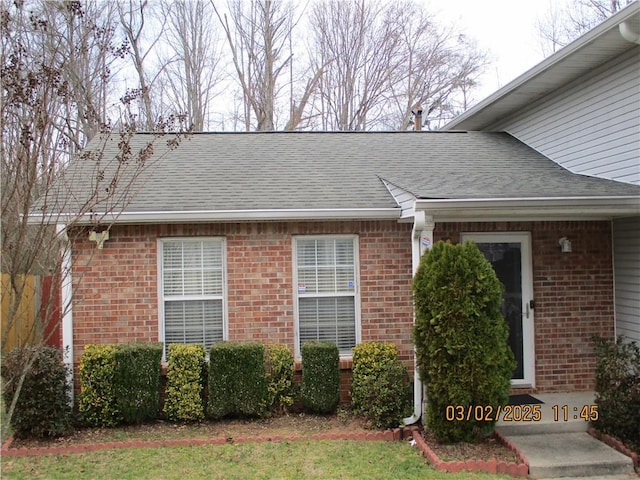 entrance to property with a shingled roof and brick siding