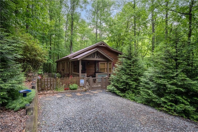 view of outbuilding featuring a gate, a porch, a fenced front yard, and a wooded view