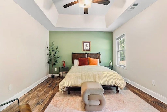 bedroom with visible vents, baseboards, a tray ceiling, wood finished floors, and a ceiling fan