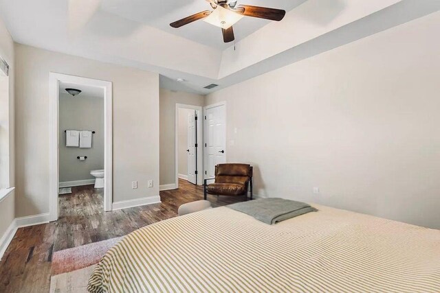 bedroom featuring wood finished floors, visible vents, baseboards, a tray ceiling, and connected bathroom