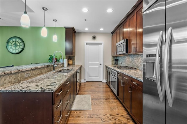 kitchen with sink, light stone counters, decorative light fixtures, stainless steel appliances, and backsplash