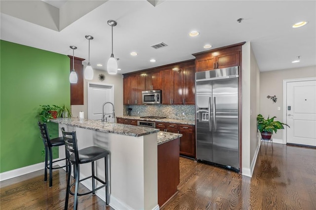 kitchen with hanging light fixtures, a kitchen breakfast bar, kitchen peninsula, stainless steel appliances, and light stone countertops