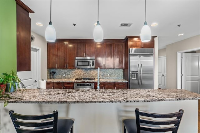 kitchen with tasteful backsplash, decorative light fixtures, light stone countertops, and appliances with stainless steel finishes