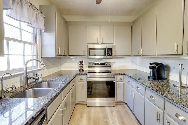 kitchen with stainless steel appliances, light hardwood / wood-style floors, stone countertops, backsplash, and sink