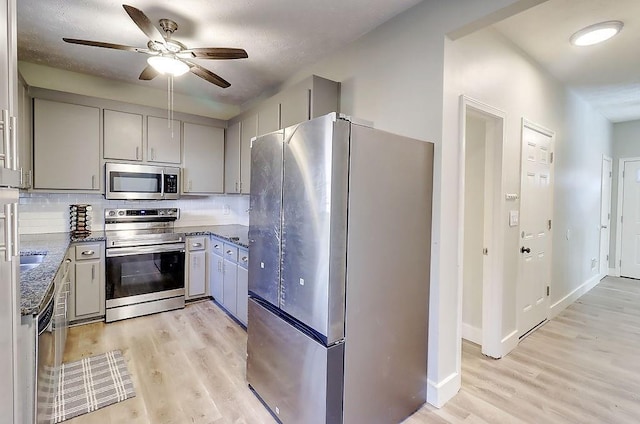 kitchen featuring appliances with stainless steel finishes, gray cabinetry, ceiling fan, light hardwood / wood-style flooring, and tasteful backsplash