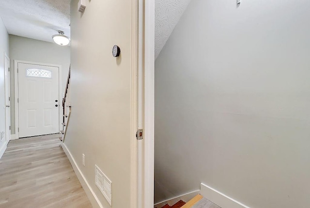 hall with a textured ceiling and light hardwood / wood-style floors