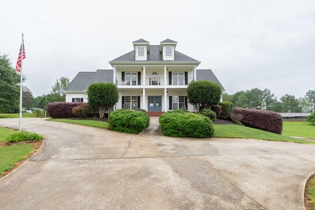 view of front facade with a porch, a balcony, a front yard, and french doors