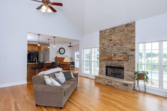 living room with high vaulted ceiling, a fireplace, light hardwood / wood-style floors, and a healthy amount of sunlight