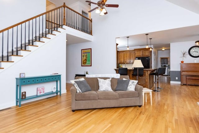 living room featuring a high ceiling, ceiling fan, and light wood-type flooring