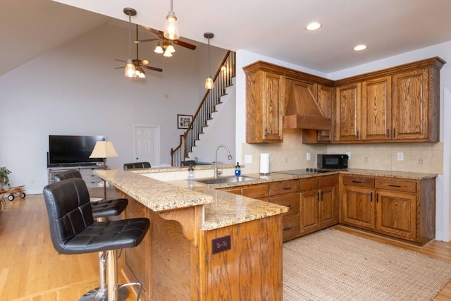 kitchen with black appliances, sink, wall chimney range hood, and kitchen peninsula