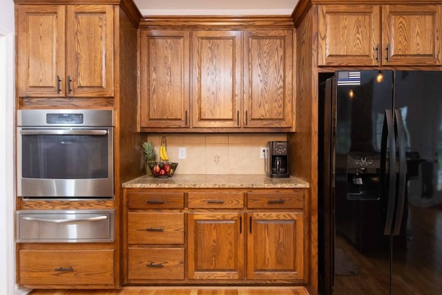 kitchen with decorative backsplash, oven, light stone counters, and black refrigerator with ice dispenser