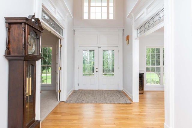 foyer with a high ceiling, light wood-type flooring, and french doors