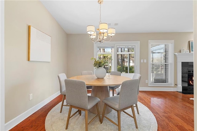 dining space with a fireplace with flush hearth, wood finished floors, baseboards, and a chandelier