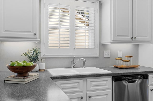 kitchen with tasteful backsplash, dark countertops, stainless steel dishwasher, white cabinetry, and a sink