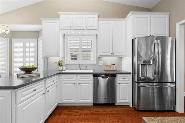 kitchen featuring dark countertops, appliances with stainless steel finishes, a peninsula, and lofted ceiling