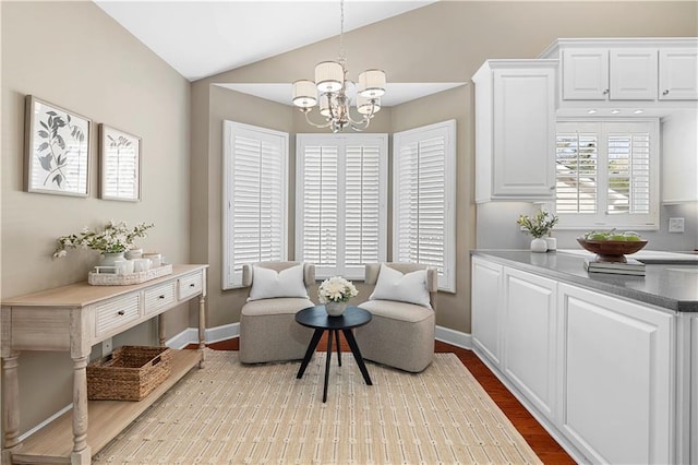 sitting room with a chandelier, vaulted ceiling, baseboards, and wood finished floors