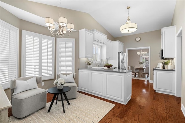 kitchen featuring wood finished floors, stainless steel appliances, a peninsula, lofted ceiling, and a chandelier