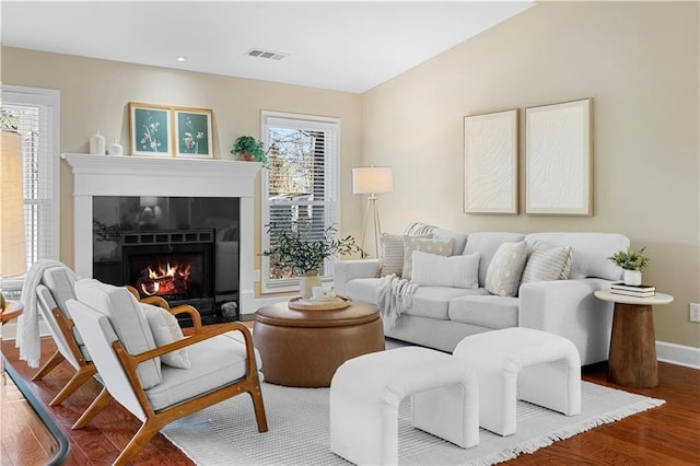 living room featuring wood finished floors, visible vents, a warm lit fireplace, and baseboards