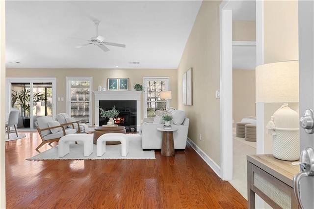 living room featuring a ceiling fan, wood finished floors, visible vents, baseboards, and a tiled fireplace