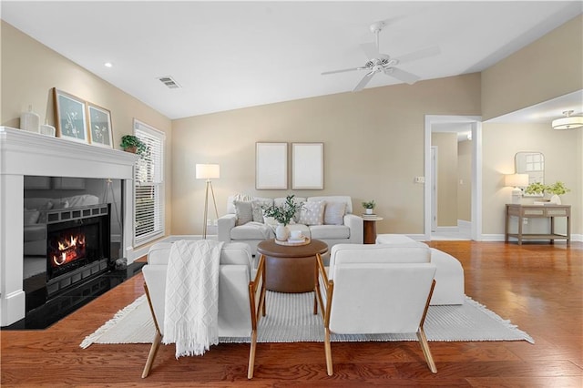 living area featuring a ceiling fan, wood finished floors, baseboards, lofted ceiling, and a tile fireplace