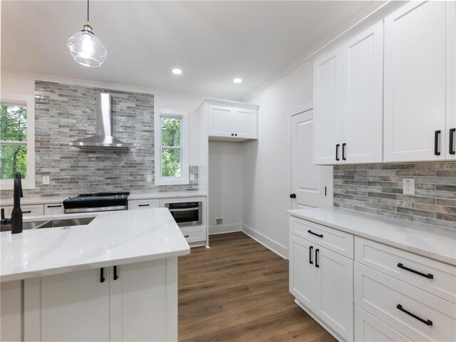 kitchen with white cabinetry, wall chimney range hood, decorative backsplash, appliances with stainless steel finishes, and decorative light fixtures