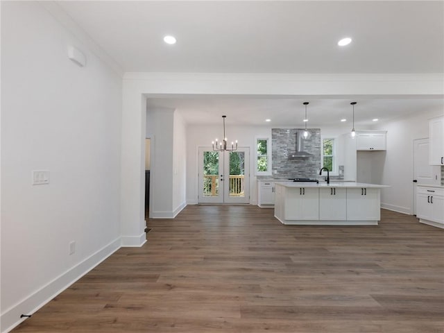 kitchen featuring a kitchen island with sink, white cabinetry, wall chimney range hood, decorative light fixtures, and dark hardwood / wood-style flooring