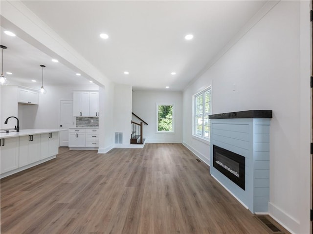 unfurnished living room featuring wood-type flooring, ornamental molding, and sink