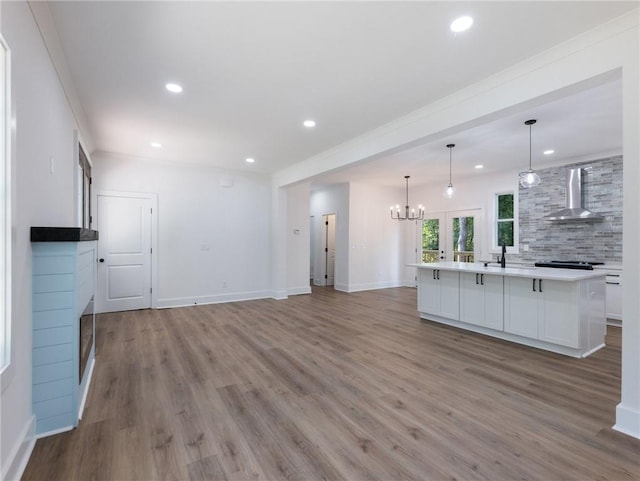 kitchen with white cabinetry, light wood-type flooring, crown molding, decorative light fixtures, and wall chimney range hood