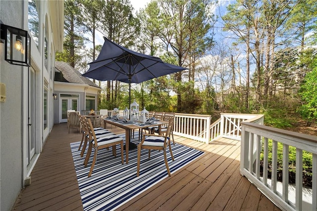 wooden terrace with outdoor dining area, french doors, and view of scattered trees