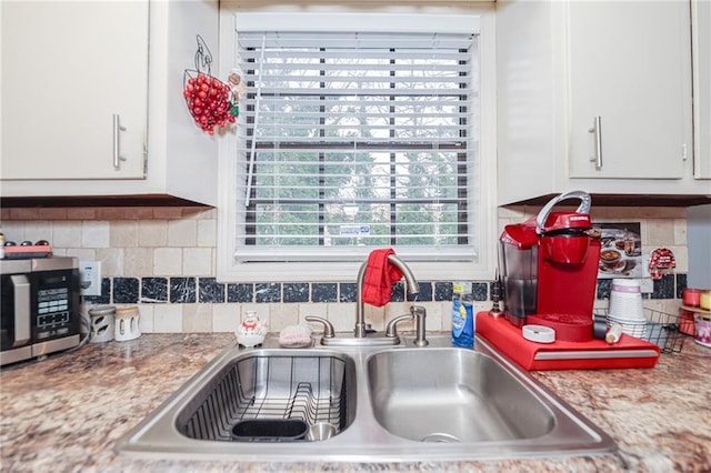 kitchen with a sink, white cabinetry, light countertops, decorative backsplash, and stainless steel microwave