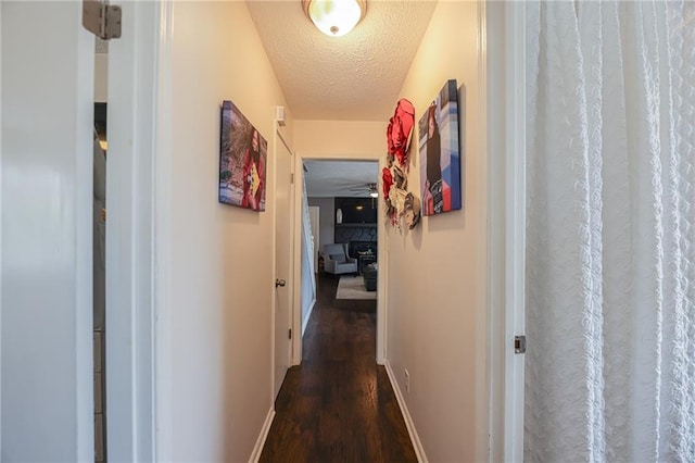 hallway with dark wood-style flooring, a textured ceiling, and baseboards