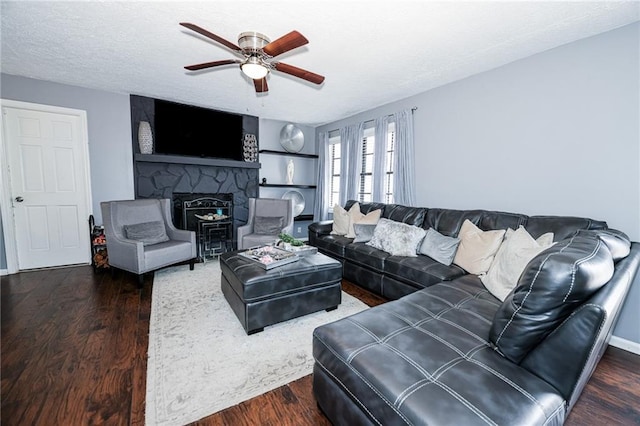 living room with a textured ceiling, ceiling fan, a stone fireplace, and wood finished floors