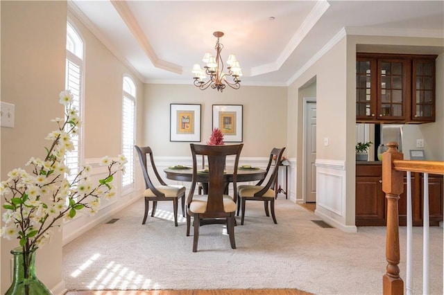 carpeted dining area with a notable chandelier, crown molding, and a raised ceiling