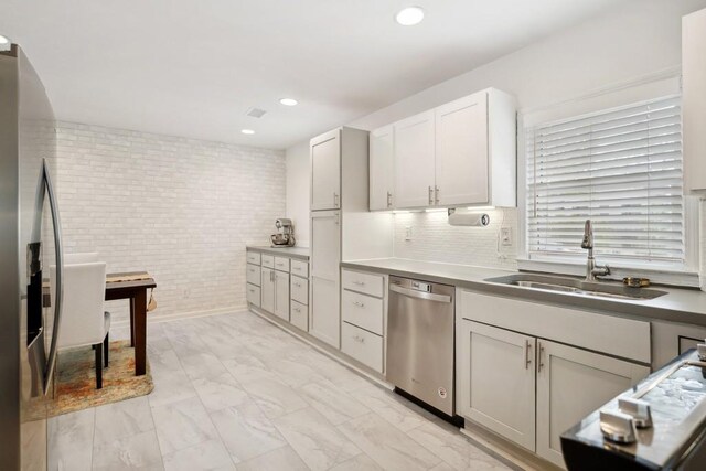 kitchen featuring white cabinets, stainless steel appliances, brick wall, and sink