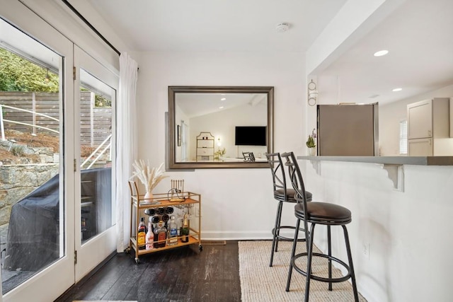 bar with dark wood-type flooring, lofted ceiling, and stainless steel refrigerator