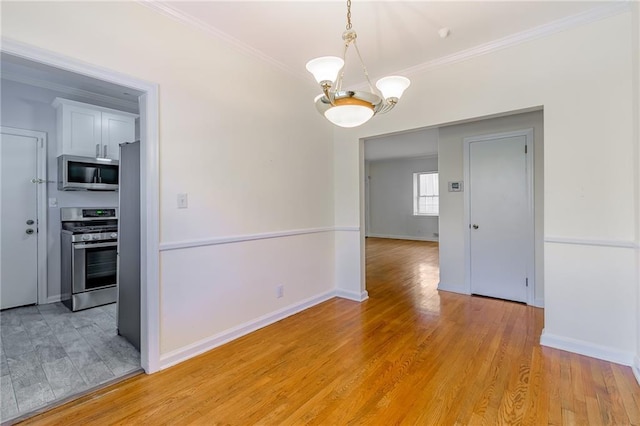 empty room featuring a chandelier, light wood-style flooring, baseboards, and ornamental molding