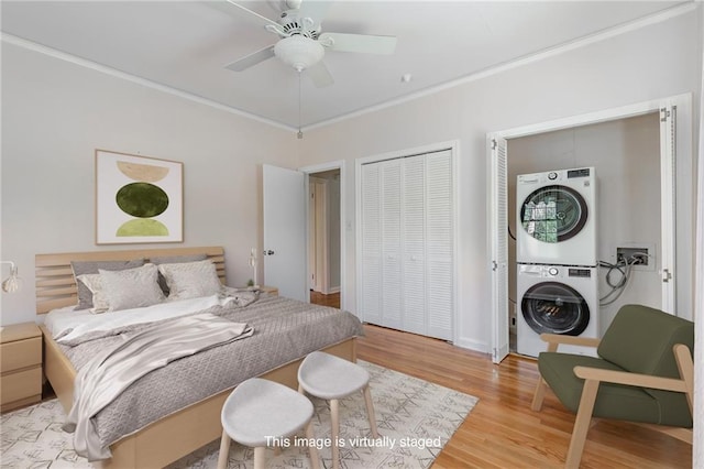 bedroom with light wood finished floors, stacked washer / dryer, ceiling fan, ornamental molding, and a closet