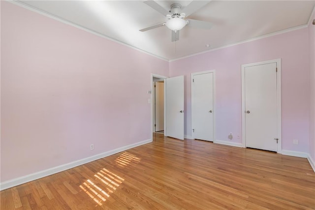 unfurnished bedroom with a ceiling fan, baseboards, light wood finished floors, ornamental molding, and multiple closets