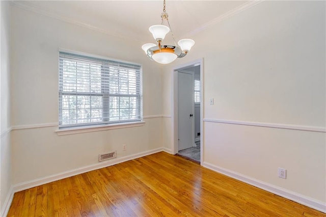 spare room with visible vents, baseboards, ornamental molding, an inviting chandelier, and wood finished floors