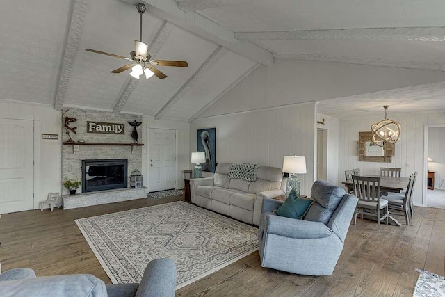 living room featuring hardwood / wood-style flooring, a stone fireplace, vaulted ceiling with beams, and ceiling fan with notable chandelier